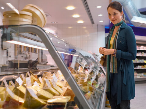 Woman shopping for cheese in a supermarket deli section with a display of various cheeses. Germany