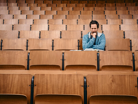 Man in a blue sweater sitting and studying in a large empty wooden lecture hall. Germany