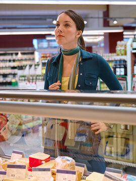 Woman with a scarf shopping in a cheese aisle at a grocery store. Germany