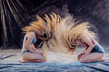 Two women kneeling with hair flipping dramatically against a dark fabric background. WA, USA