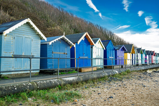 Colorful beach huts lined along a seaside boardwalk with a bright blue sky above. Norfolk,Cromer, England