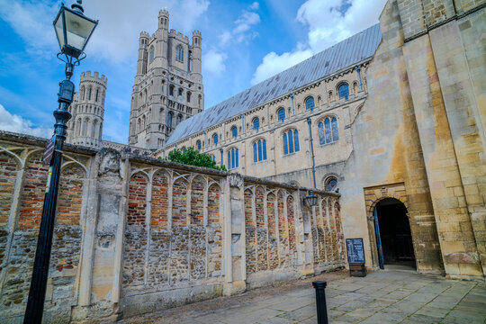 Historic cathedral with tall towers under a blue sky, seen from a cobblestone street angle. Ely, England