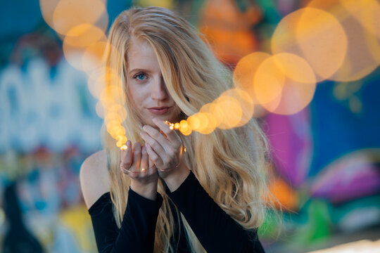 Young woman with long blonde hair holding string lights against colorful graffiti backdrop. WA, USA