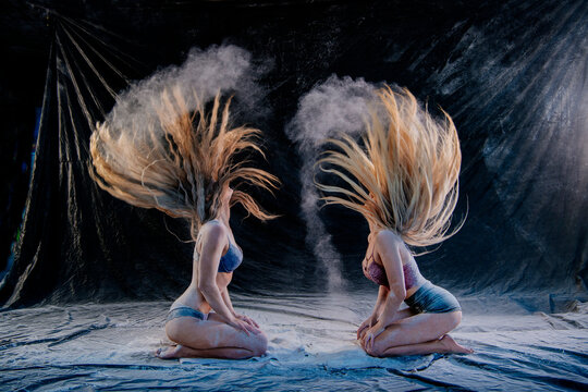 Two women kneel on fabric, flipping hair as powder creates dynamic patterns in the air. WA, USA