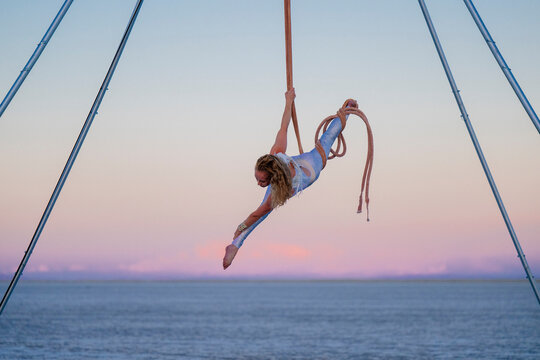 Aerial performer suspended over the ocean at sunset, showcasing impressive acrobatics. WA, USA