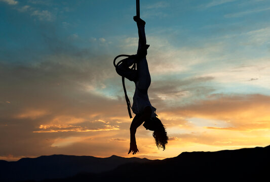 Silhouette of aerial performer hanging upside down against a vibrant sunset sky. WA, USA