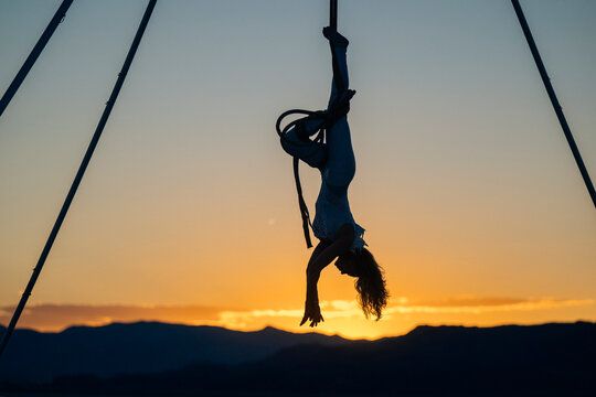 Aerial performer hanging upside down at sunset, silhouetted against a glowing sky and mountains. WA, USA