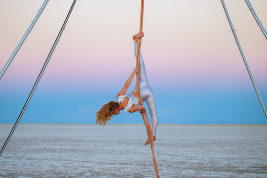 Aerial performer in silver outfit balances gracefully on a rope against a pastel sky. WA, USA