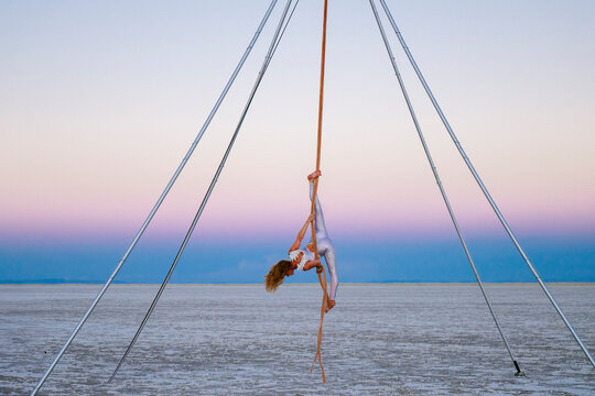 Aerial performer gracefully hangs upside down on a pole in a vast, serene desert landscape. WA, USA