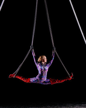 Aerial performer doing splits on chains in dramatic lighting with red boots. WA, USA