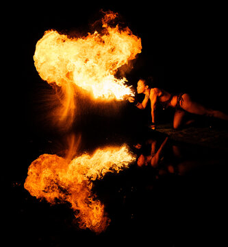 Fire breather blowing flames, reflected on water in a dramatic night setting.   WA, USA