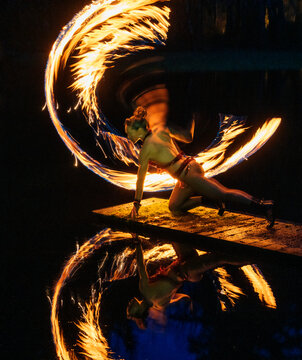 Performer spins fire poi creating luminous trails against a dark backdrop, reflected in water. WA, USA