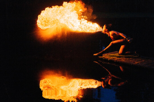 A fire performer breathes flames over a dark body of water at night. WA, USA