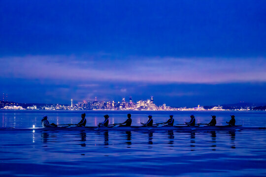 Rowers glide on calm water with a city skyline glowing in the blue evening light. WA, USA