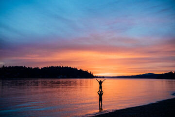 Silhouette of two people at sunset by a calm lake with vibrant sky colors. WA, USA