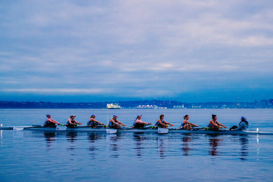 Rowing team glides on calm water under a cloudy sky during twilight hour. WA, USA
