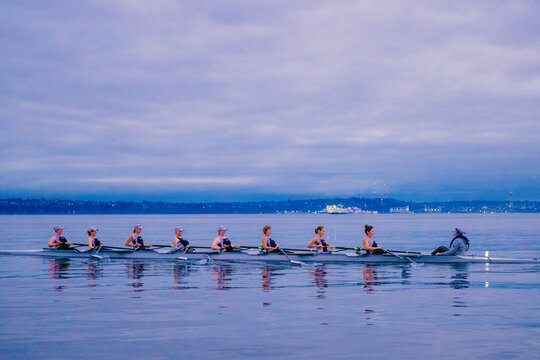 A rowing team practices on calm water under a cloudy purple-blue sky at dawn. WA, USA