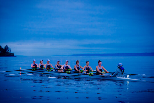 A team of rowers glides across calm waters at dusk, showcasing teamwork and synchronization. WA, USA