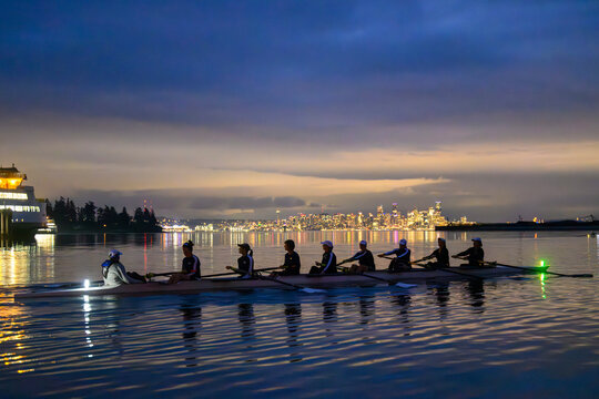 Rowers glide on calm water with a city skyline glowing at dusk under a cloudy sky. WA, USA