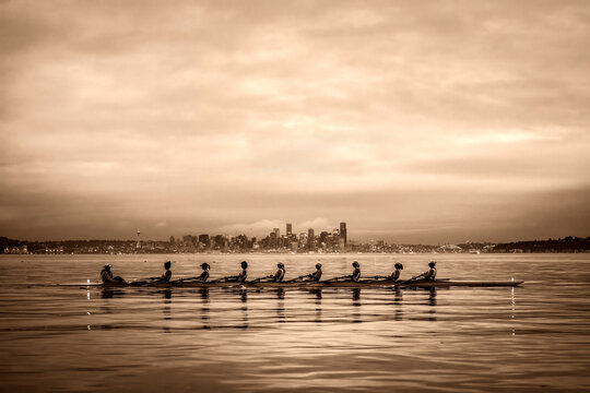 Rowing team on calm water with a city skyline in the background under a cloudy sky. WA, USA