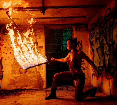A performer crouches with a flaming torch in a graffitied, industrial setting. WA, USA