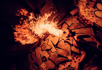 Fire performer breathes flames in front of vibrant graffiti underpass at night. WA, USA