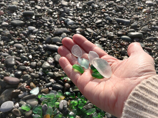Woman put glass sea pebbles of different colours on shore, beach. Nature and ecology. Background for design.