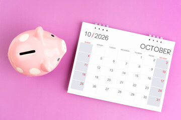 Desk calendar for October 2026 and pink piggy bank on purple background.