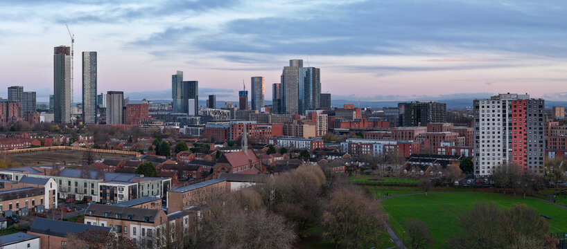 Aerial panorama showcasing the historic St Clement&rsquo;s Church in Salford and the expansive Ordsall residential district, set against the towering glass skyscrapers of Manchester