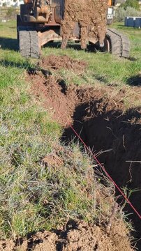 The bucket of a mini backhoe digging the earth and preparing the trench for a foundation.