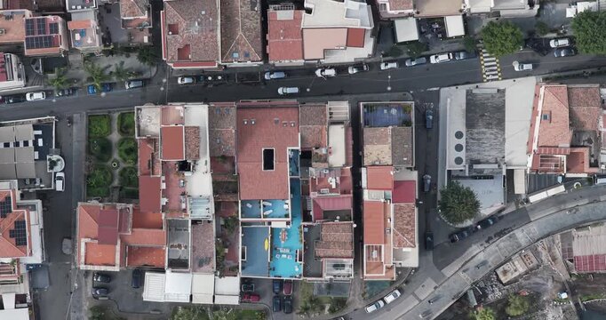 Aerial view of buildings with red roofs and roads filled with cars creating a vibrant contrast, Aci Trezza, Sicily, Italy.