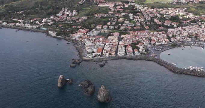 Aerial view of the dramatic Faraglioni rocks rising from the cobalt sea near the charming coastal town, Aci Trezza, Sicily, Italy.