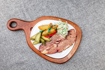 Beef brisket steak with baked potatoes. It is served in a white plate on a wooden cutting board....