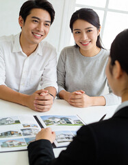 Young asian couple and real estate agent sitting at table and looking at camera