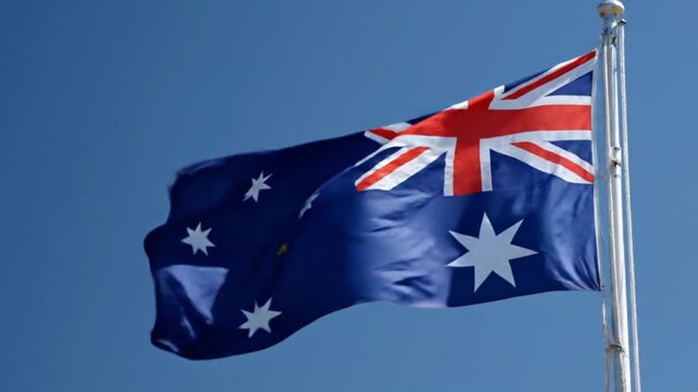 A vibrant blue flag, adorned with a prominent red, white, and blue rectangular pattern in its upper left quadrant and several distinct white stars across its field, gracefully billows against a brilli