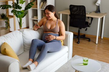 Pregnant woman relaxing on couch using phone