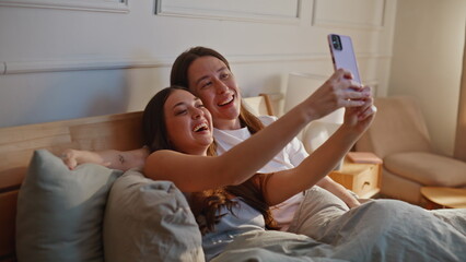 Laughing lovers taking selfie using phone in bedroom enjoying morning closeup