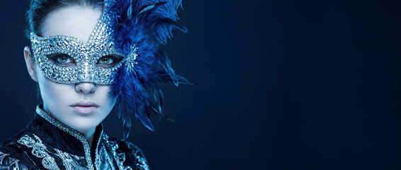 Beautiful woman in luxury Venetian mask with blue feathers and diamonds. Mysterious masquerade carnival portrait on dark background with copy space.