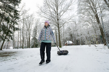 Girl pulling inflatable donut sled through a scenic snowy winter park.