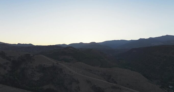 Drone aerial of Granada foothill ridge at sunrise, warm autumn light washing over rolling hills and the city beyond, Andalusia Spain