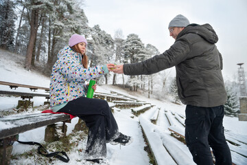 Girl gives a mug of hot drink from a thermos to a man in a snowy winter park