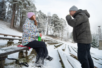 Man and a woman drinking a hot drink from a thermos mug in a snowy winter park