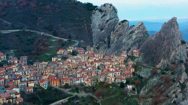 Aerial view of Castelmezzano village nestled between jagged Dolomiti Lucane mountains, its red-roofed buildings contrasting with the rocky landscape, Castelmezzano, Basilicata, Italy.