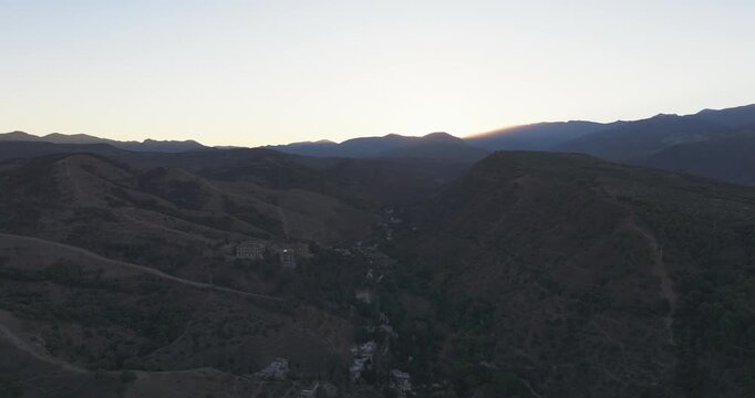 Aerial drone across Granada foothill slopes at dawn, sunrise glow skimming over the hills and city beyond, Andalusia Spain