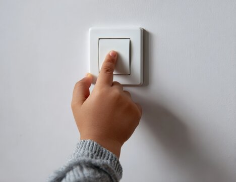 Hispanic child's hand pressing light switch on white wall