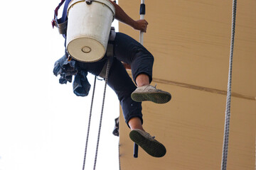 Professional rope access window cleaner working at height on building exterior using safety harness and bucket, high-rise maintenance service concept