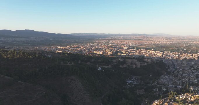 Aerial drone view across Granada at sunrise, warm autumn glow and long shadows over foothills with Alhambra area nearby, Andalusia Spain