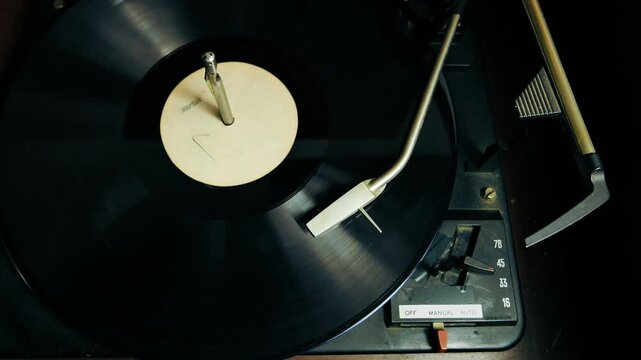 A vinyl record spins on a vintage record player turntable, white label, with the stylus down. Music album spinning with the needle cartridge.