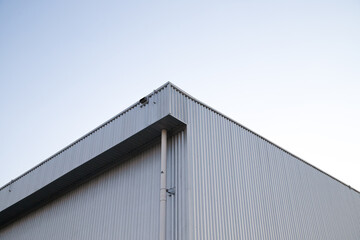 Warehouse Factory Industry Building with Geometric Metal Corrugated Steel Wall and Rooftop against Blue Sky Background, Modern Industrial Exterior Architecture Backdrop Structure in Minimal Style