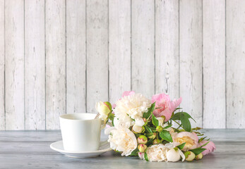 White cup of coffee or tea and bouquet of white peony flowers on a wooden table agaisnt white wooden background